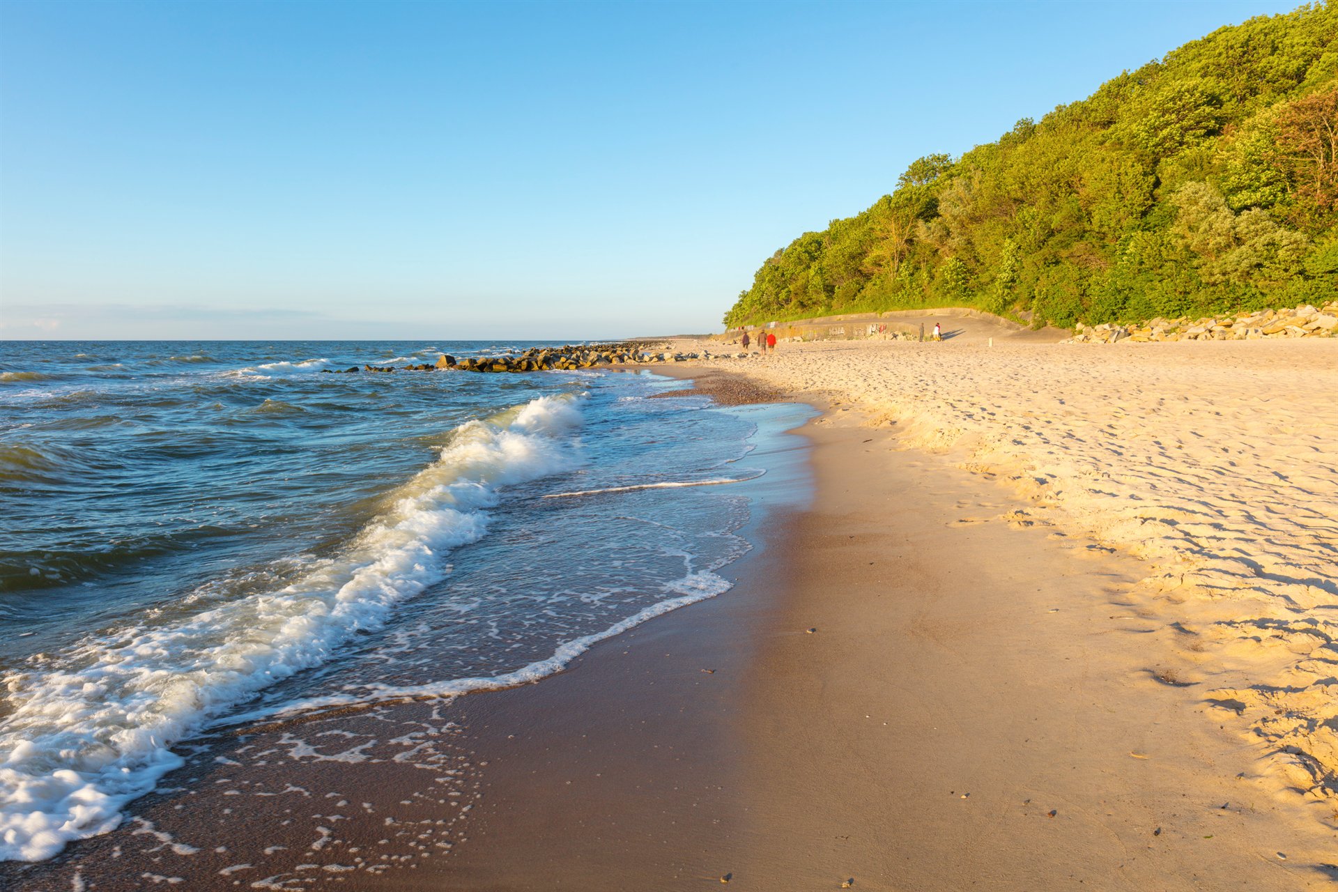 Słoneczna plaża z falami, piaszczystym brzegiem i zielonym klifem w tle