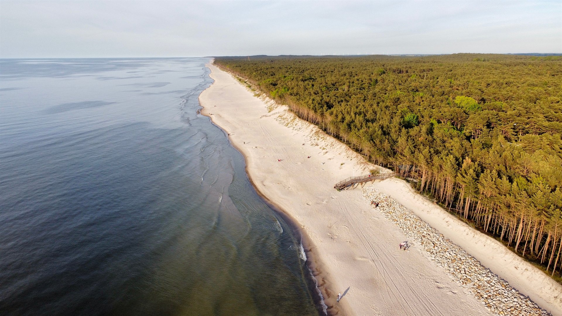 Piaszczysta plaża z lasem, spokojne morze i drewniana kładka widziane z lotu ptaka