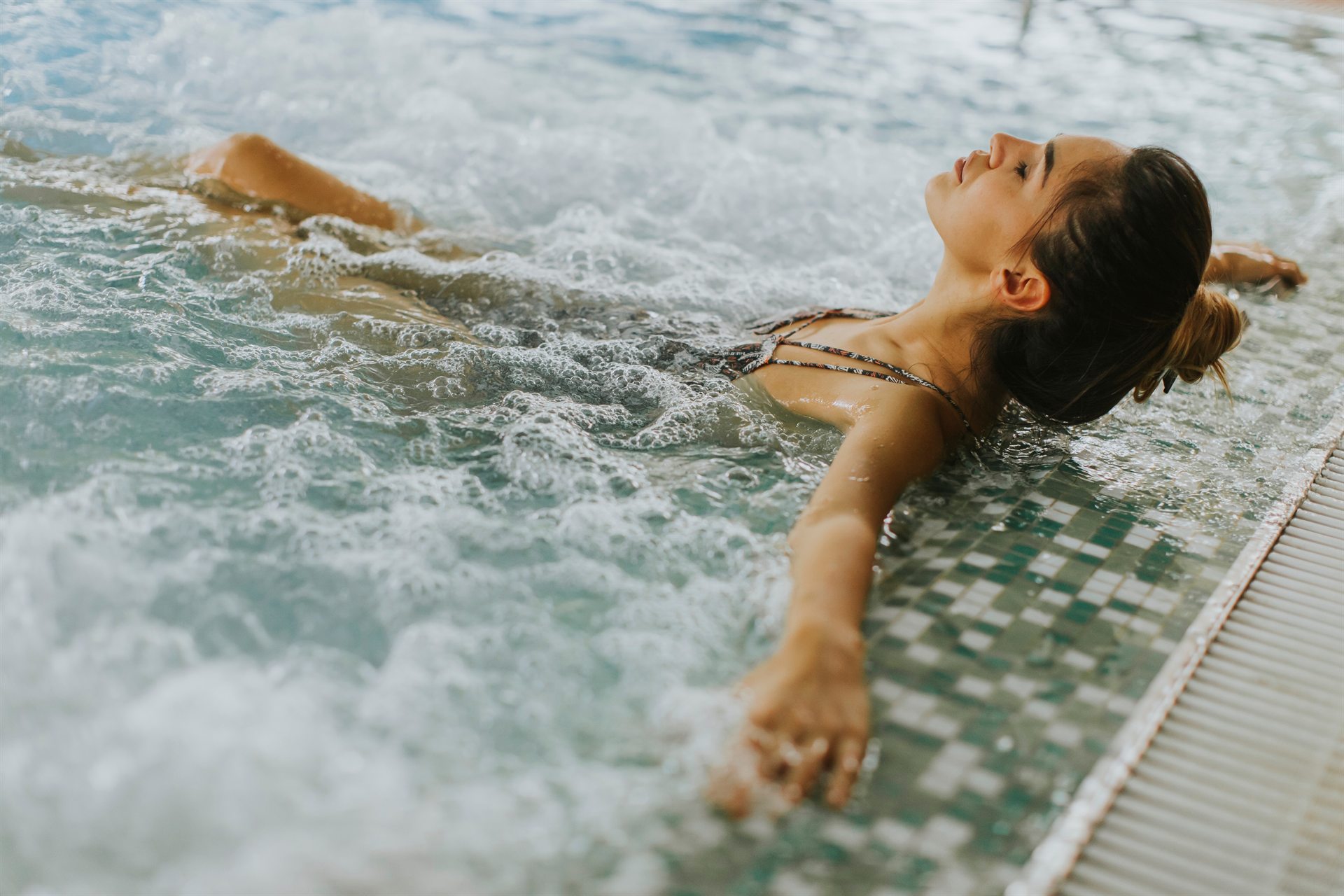 Kobieta relaksuje się w jacuzzi, leżąc na wodzie z zamkniętymi oczami i rozłożonymi rękami