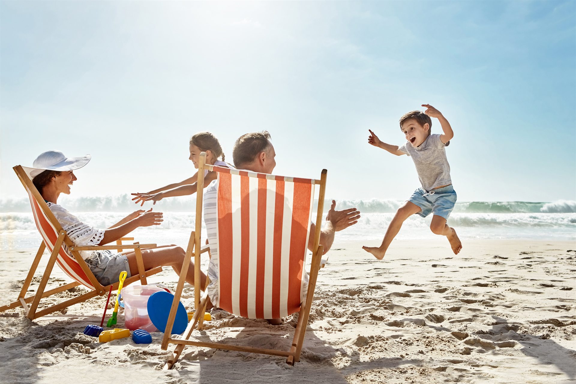 Rodzina na plaży: dzieci bawią się przy leżakach, a chłopiec skacze radośnie na piasku