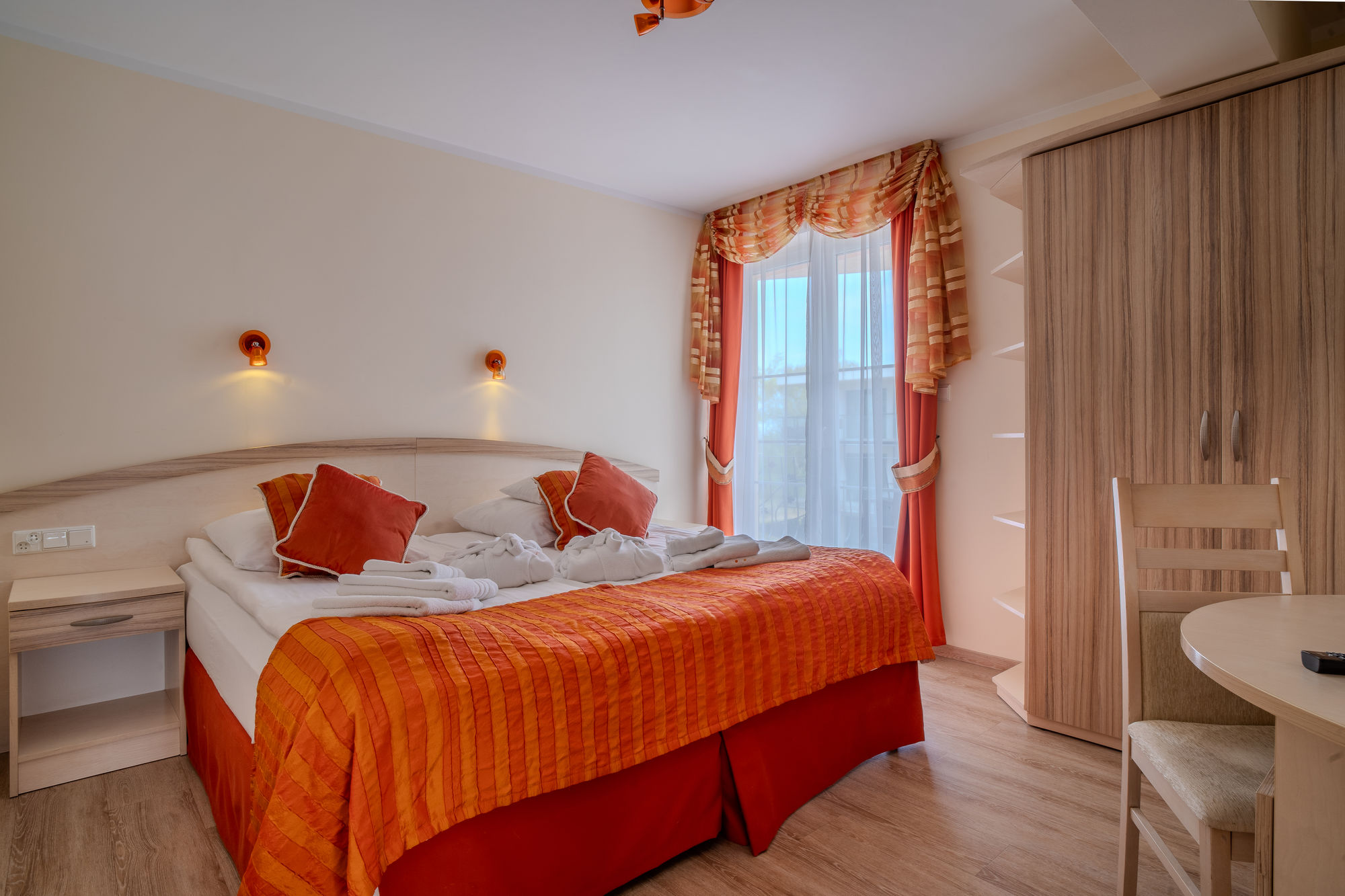 Przytulny pokój hotelowy z łóżkiem, pomarańczową narzutą, szafą, biurkiem i oknem z zasłonami
