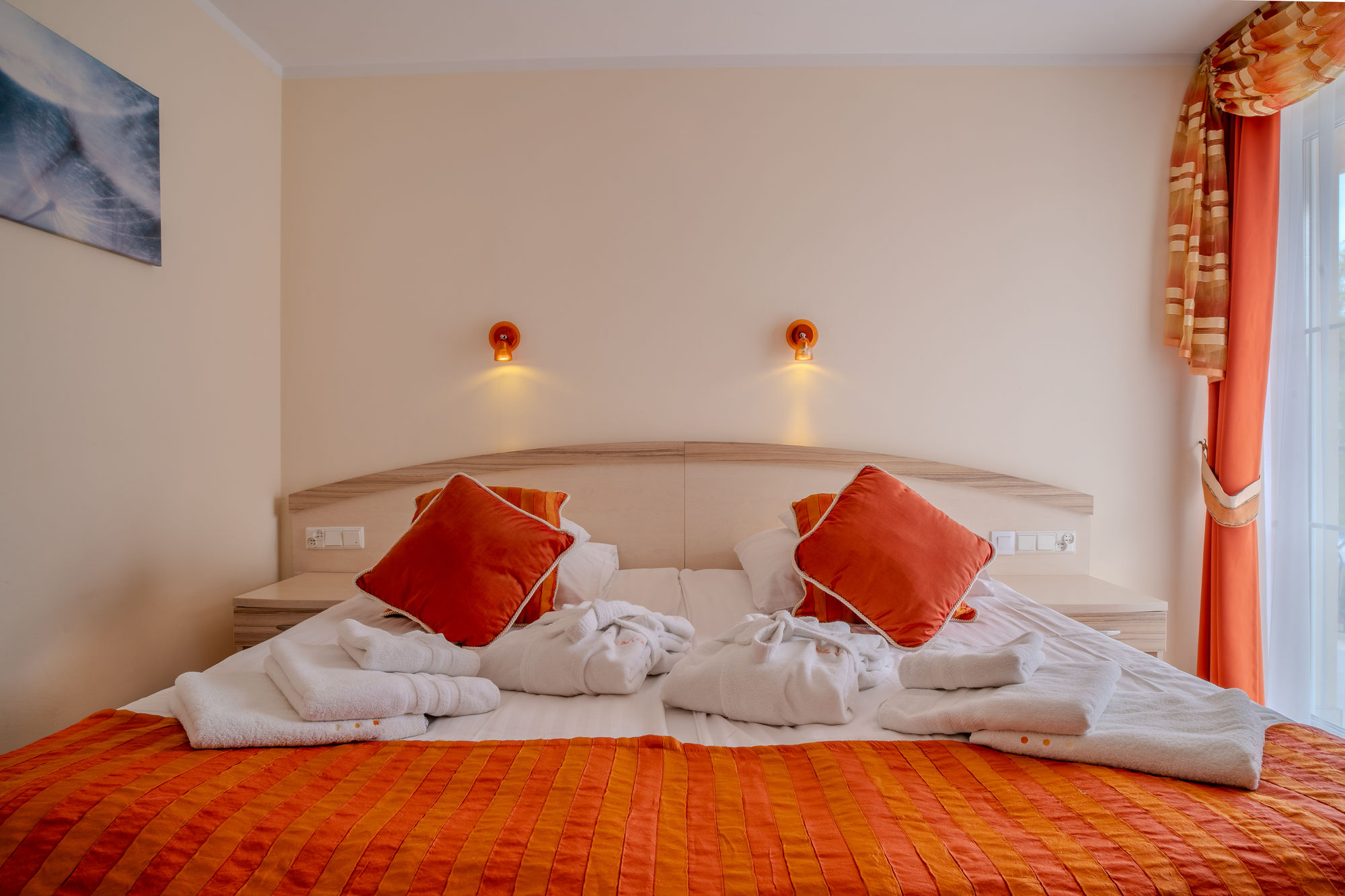 Przytulne łóżko w hotelowym pokoju z pomarańczową narzutą, poduszkami i ręcznikami na narzutach
