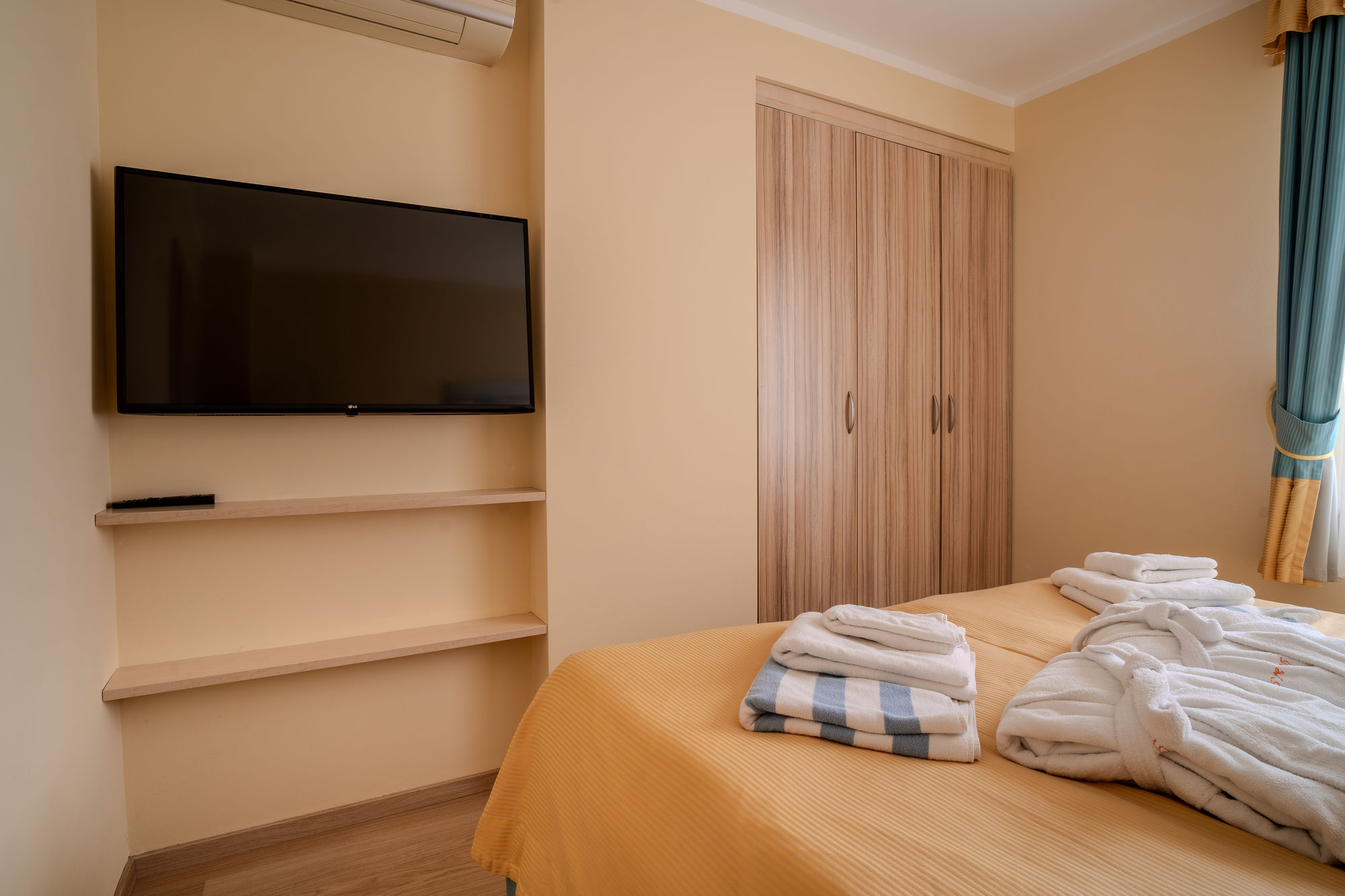 Jasny pokój hotelowy z łóżkiem, telewizorem, szafą i ręcznikami na pościeli