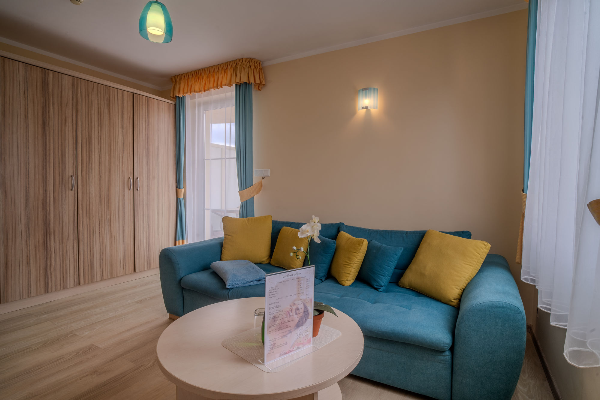 Jasny salon z turkusową sofą, żółtymi poduszkami, okrągłym stołem i drewnianą szafą
