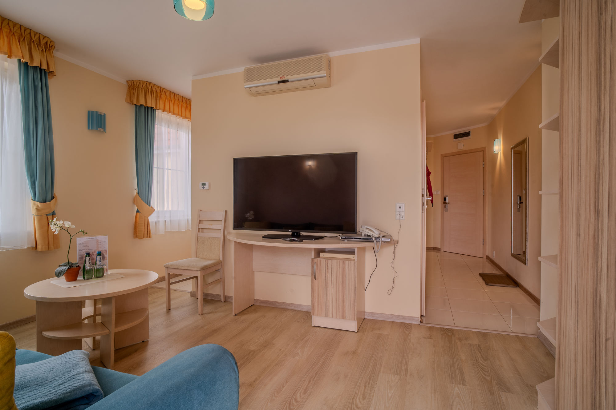 Jasny pokój hotelowy z telewizorem, stołem, krzesłem, klimatyzacją i widokiem na korytarz