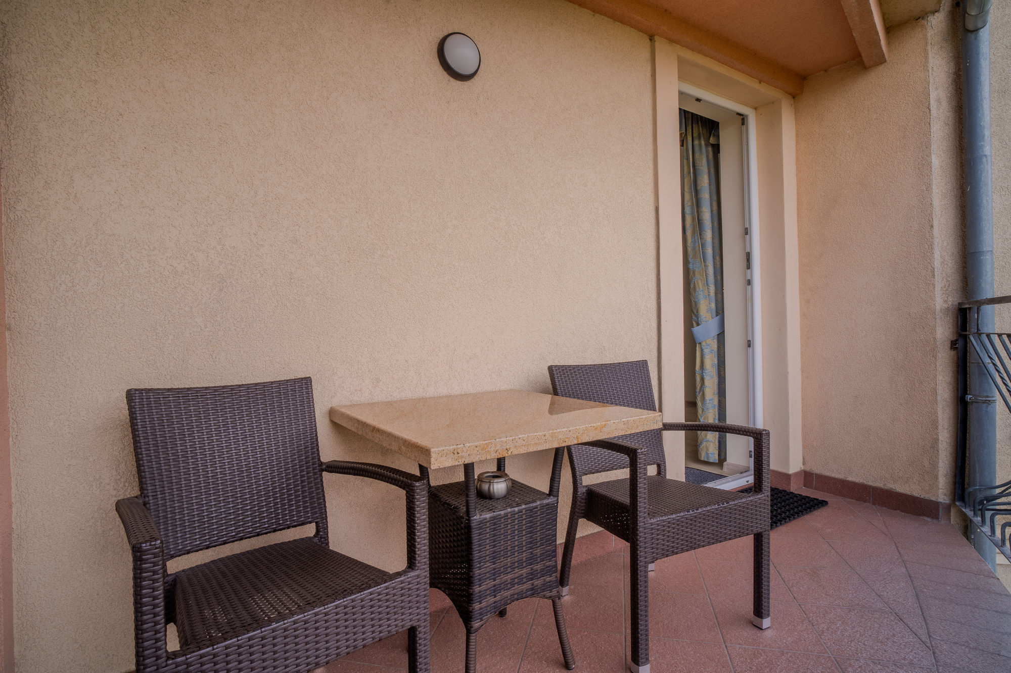 Taras z dwoma wiklinowymi fotelami, stolikiem i otwartymi drzwiami na balkon