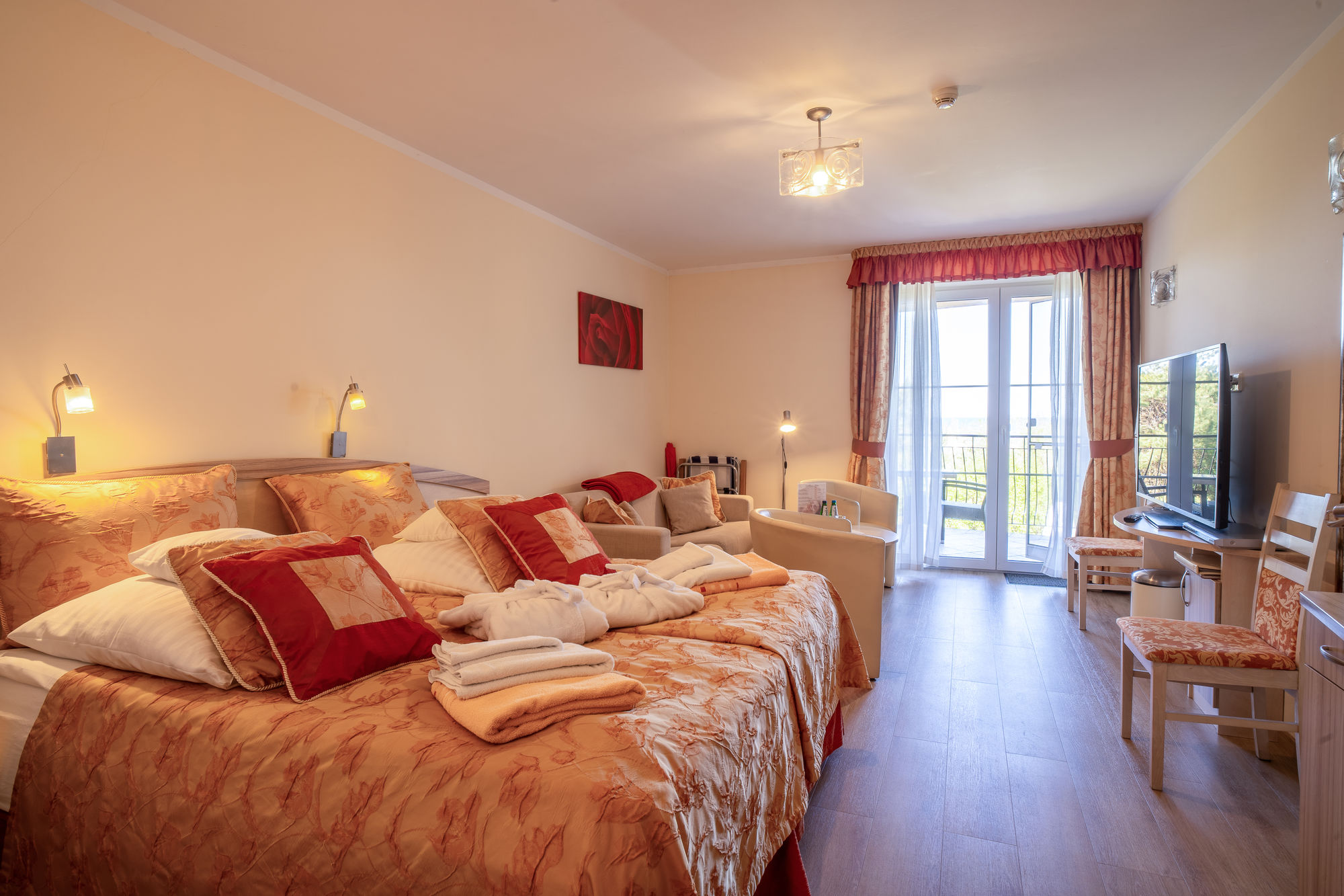 Jasny pokój hotelowy z dużym łóżkiem, kanapą, telewizorem i balkonowymi drzwiami