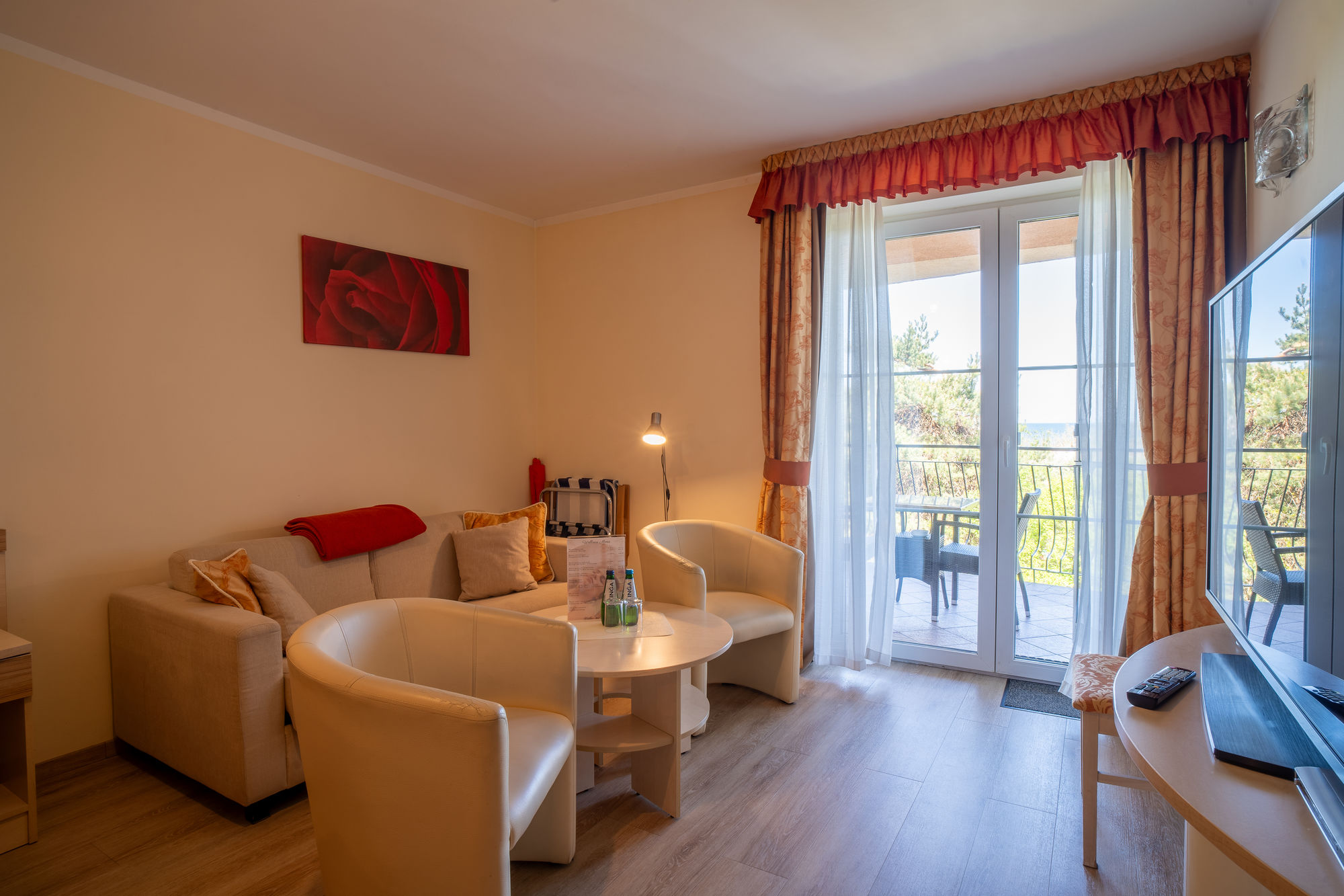 Jasny salon z beżową sofą, białymi fotelami, stolikiem i balkonem z widokiem na zieleń
