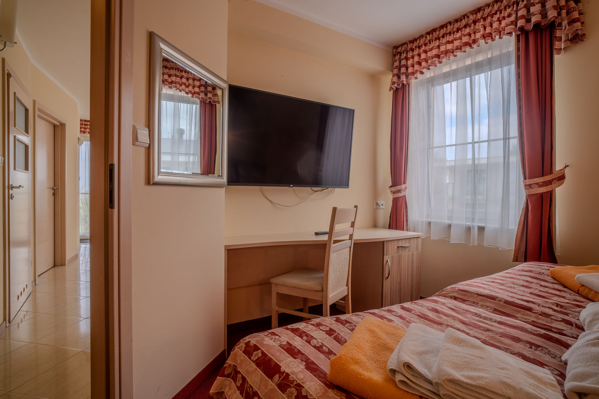 Jasny pokój hotelowy z łóżkiem, biurkiem, telewizorem i dużym oknem z zasłonami