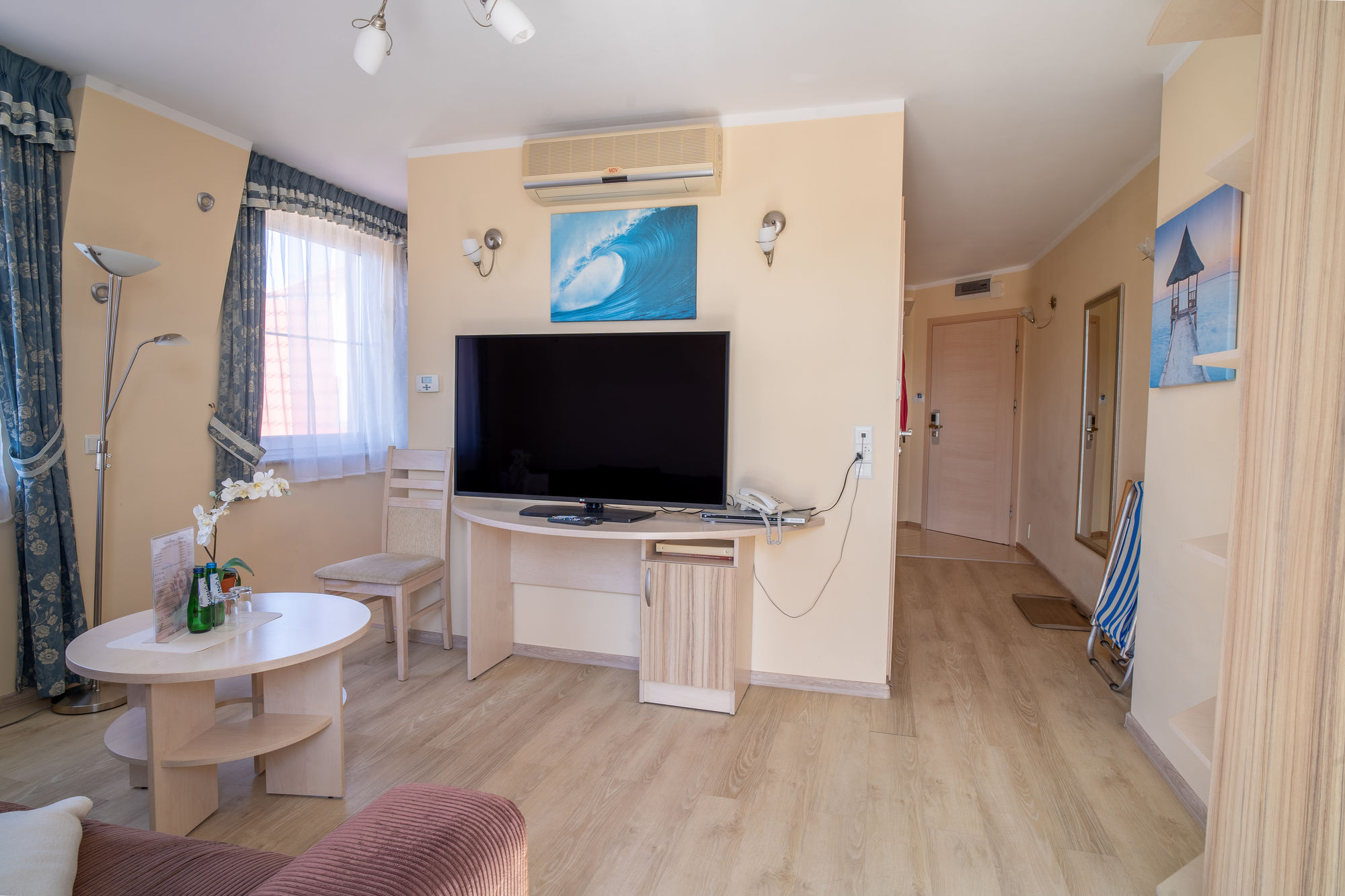 Jasny pokój hotelowy z telewizorem, stołem, krzesłem i zdjęciami fal na ścianach