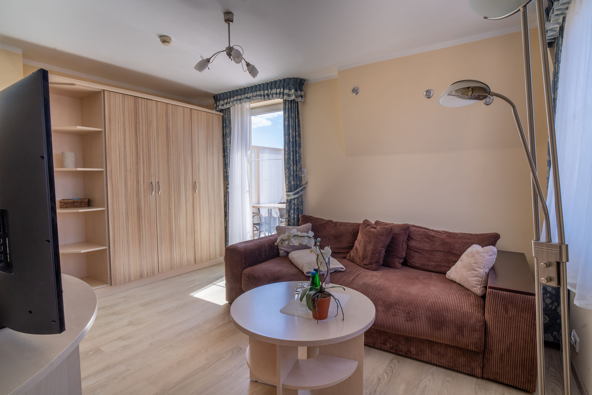 Przytulny salon z brązową sofą, okrągłym stolikiem, szafą i dużym oknem