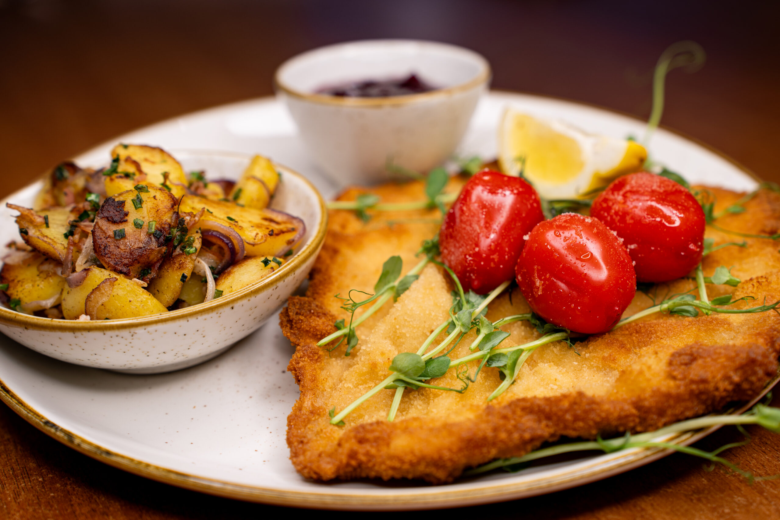 Smażony kotlet z pomidorkami, mikroliśćmi, ziemniakami i miską pieczonych warzyw